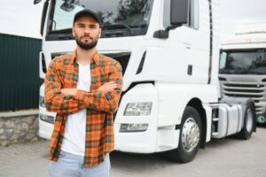 A portrait captures a young, bearded trucker standing proudly beside his vehicle, embodying the essence of transportation service and the essential role of a truck driver.